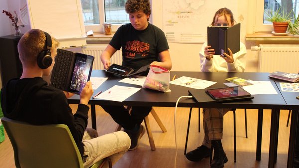 Jugendliche sitzen an Tisch und probieren mit Tablets AR aus